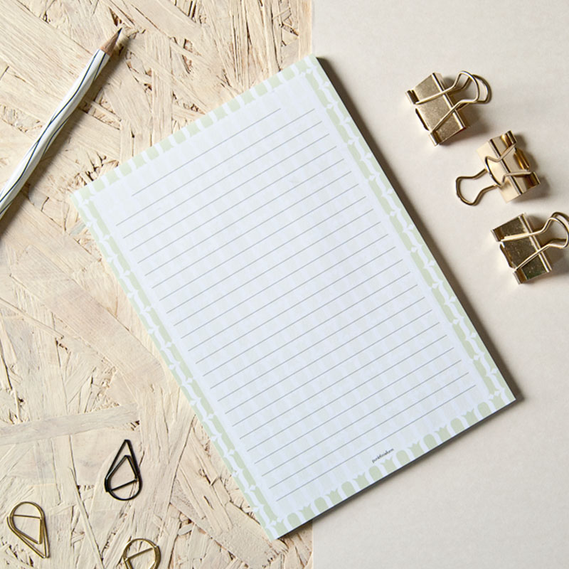 Zu sehen ist ein Notizblock mit einem grünen Tulpenmuster. Das Muster umrahmt die Schreiblinien.